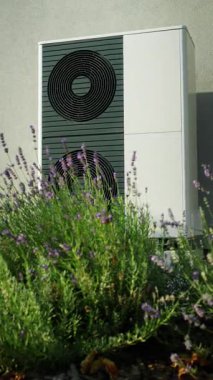 Hava kaynağı ısı pompası çiçek açan bahçe çalılarının yanında gün ışığında kelebeklerle.