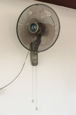 Duvara monte edilmiş elektrikli vantilatör. Beyaz duvarda çekme kabloları var. Tropikal evin iç kısımlarında havalandırma ve soğutma sağlıyor..