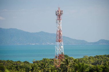 Telekomünikasyon kulesi, açık mavi gökyüzünün altında turkuaz deniz ve uzak ada tepeleriyle tropikal ormanın üzerinde yükseliyor. Yüksek kalite fotoğraf