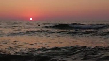 Sakin denizin üzerinde gün batımı, yumuşak dalgalar ve ışıldayan ufuklarla..