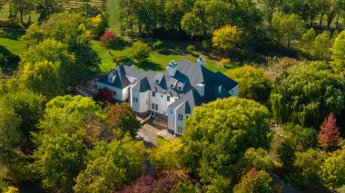 ABD 'nin New York eyaletinde sonbahar ağaçları ve kırsal alanla çevrili lüks kır köşkünün havadan görünüşü.