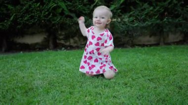 Arka bahçede yeşil çimlerde sürünen küçük kız kameraya gülümsüyor..