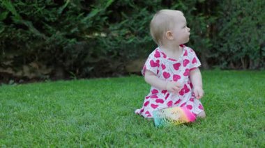 Küçük kız yeşil çimlerde renkli oyuncaklarla oynuyor ve sürünerek uzaklaşıyor.