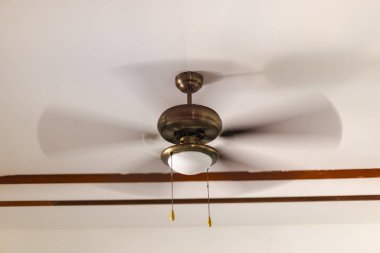 Tavan vantilatörü beyaz tavanda dönüyor. İç kısımda da aydınlatma armatürü var..