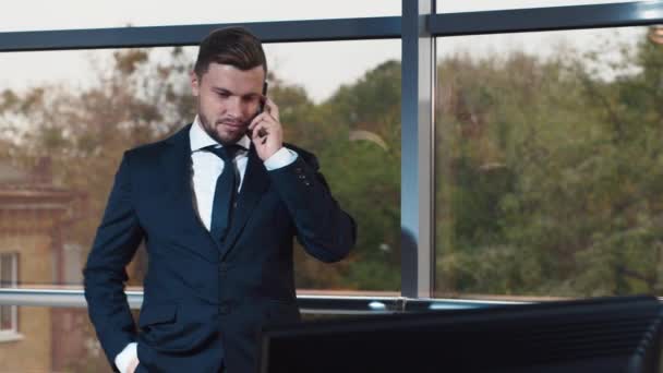 Молодой бизнесмен разговаривает по телефону у окна офиса — стоковое видео