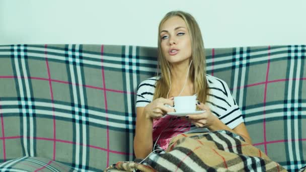 Mujer atractiva en el sofá escuchando música con auriculares — Vídeo de stock