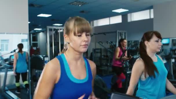 Две привлекательные девушки упражняются на беговой дорожке в спортзале — стоковое видео