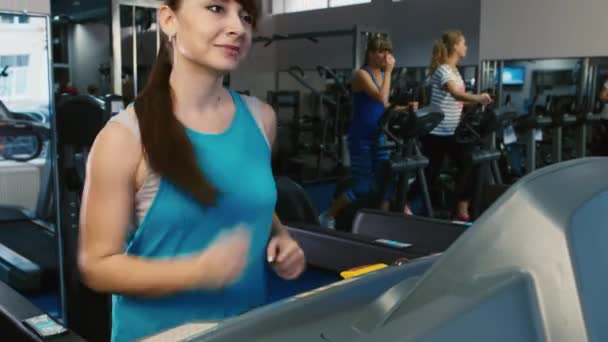 Mujer atractiva corriendo en una cinta de correr, sonriendo. Entrenamiento en el gimnasio — Vídeos de Stock