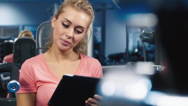 Attraktive Frau, die in einem Sportverein mit dem Tablet arbeitet — Stockvideo