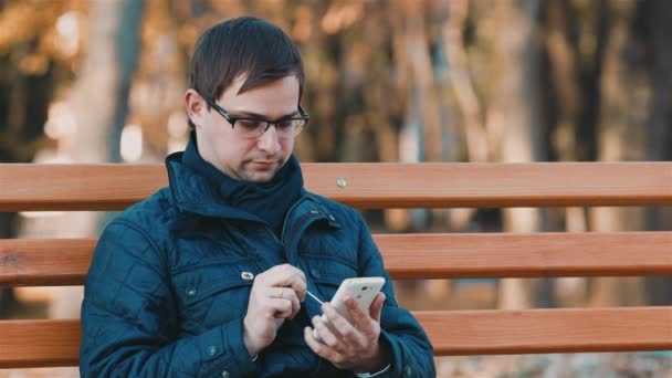 Бизнесмен работает со смартфоном в осеннем парке — стоковое видео