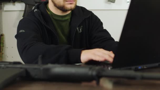 A man working at a laptop on the background of the stack of weapons — Stock Video