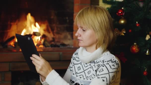 Vrouw werkt met een Tablet PC in de buurt van de open haard en de kerstboom — Stockvideo