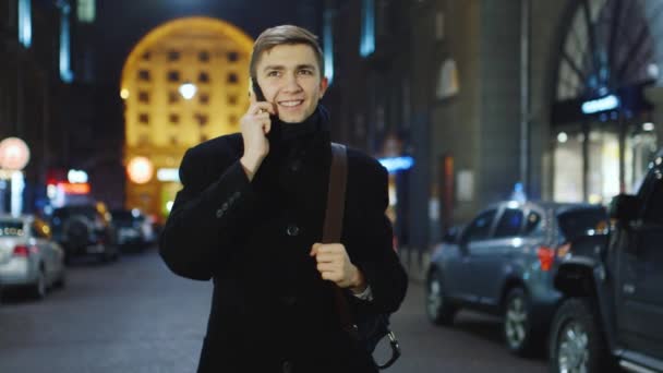 Привлекательный молодой человек разговаривает по телефону на вечерней улице — стоковое видео