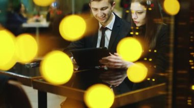 Bir kafede oturan genç çift ve tablet ekranında görünüyor