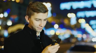Genç bir adam şehrin bir arka plan üzerinde bir cep telefonu ekran geceleri okur.