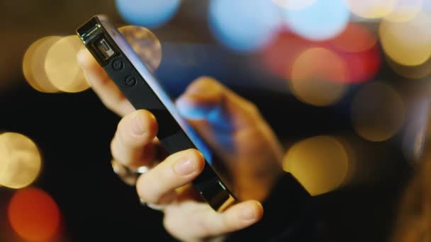 Hand with a mobile phone against a background of blurred lights — Stock Video