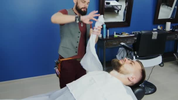 El barbero pone una toalla en su barba visitante — Vídeos de Stock