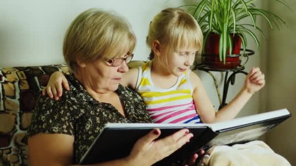 Grootmoeder met haar kleindochter kijkt een album met familiefoto 's — Stockvideo