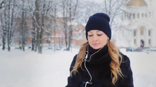 Mujer atractiva caminando en la calle en el invierno y escuchando música — Vídeo de stock