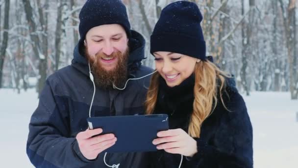 Hombre y mujer usando una tableta en el bosque de invierno, sonriendo . — Vídeos de Stock