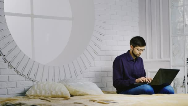 胡子的男子在眼镜坐在床上，使用一台笔记本电脑 — 图库视频影像