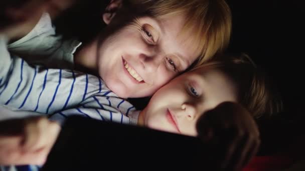 母亲和女儿享受平板电脑躺在床上在晚上 — 图库视频影像