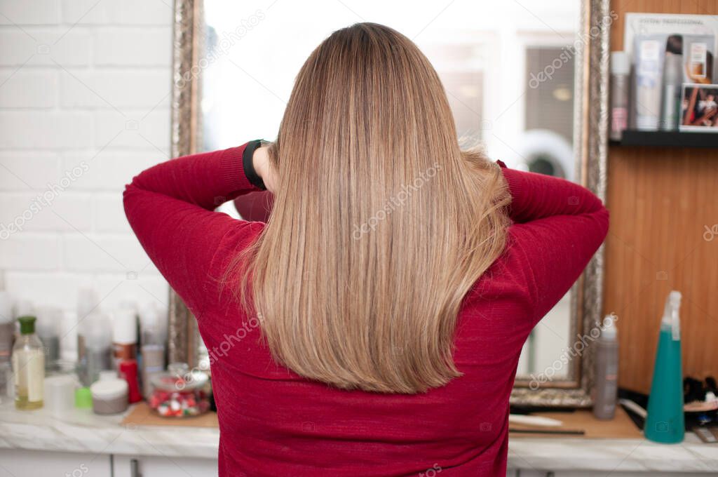 Woman with brown long hair at the mirror in a beauty salon view from the back, close-up hair