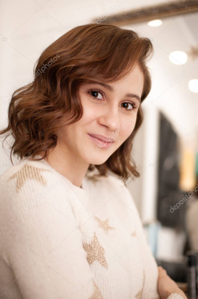 Beautiful wavy hairstyle on a young woman with medium length brown hair without cosmetics indoors close-up
