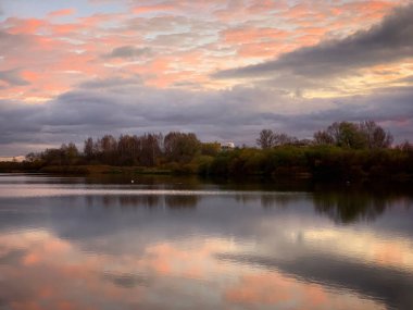 Gölde gün batımı, bulutlar ve arka planda su.