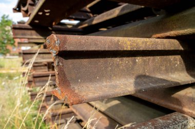 Endüstriyel depolama alanında yığılmış paslı demiryolu rayları