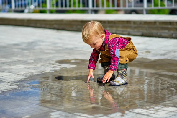 Küçük çocuk elinde bir su birikintisi ıslatıyor