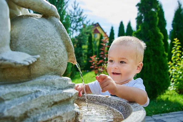 Маленький хлопчик грає з водою у фонтані — стокове фото