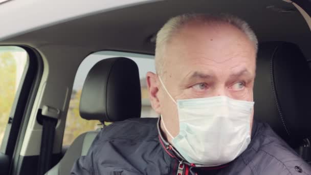En man i en bil med mask i ansiktet tittar ut genom fönstret.. — Stockvideo