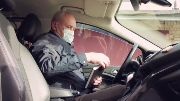 Mężczyzna z maską na twarzy w samochodzie bierze pamiętnik i zapisuje. — Wideo stockowe