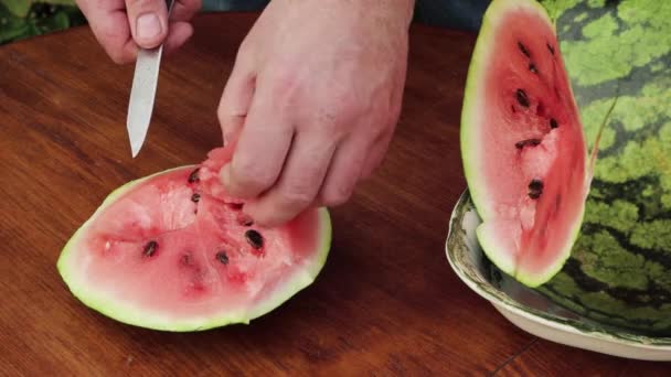 Een man snijdt roze vlees van een watermeloen met een mes. — Stockvideo