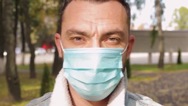 Un hombre con una máscara médica mira la cámara de cerca. — Vídeos de Stock