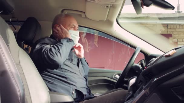 Mannen i bilen bär försiktigt en blå medicinsk mask över ansiktet. — Stockvideo