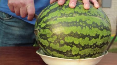 Bir adamın eli bıçakla karpuzdan yuvarlak bir dilim keser.. 