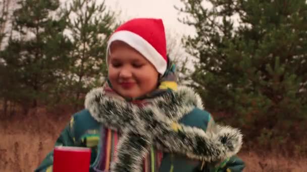 Op kerstavond heeft een jongen plezier buiten met een rode pet op.. — Stockvideo