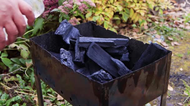 A mans hand pours a lighter fluid into a charcoal grill. — Stock Video