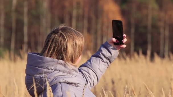 Mujer joven en la hierba alta toma fotos de sí misma en el teléfono. — Vídeo de stock