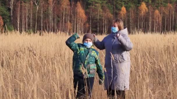 マスクのお母さんと息子は背の高い草の中で踊っている. — ストック動画