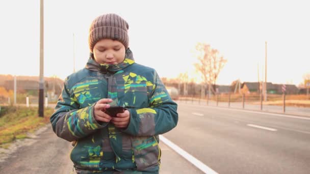 Um menino no fundo da auto-estrada fica com um telefone e mostra a classe — Vídeo de Stock