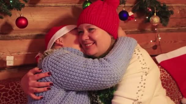 Jongen en mam in rood caps close-up veel plezier knuffelen en kussen op kerst. — Stockvideo