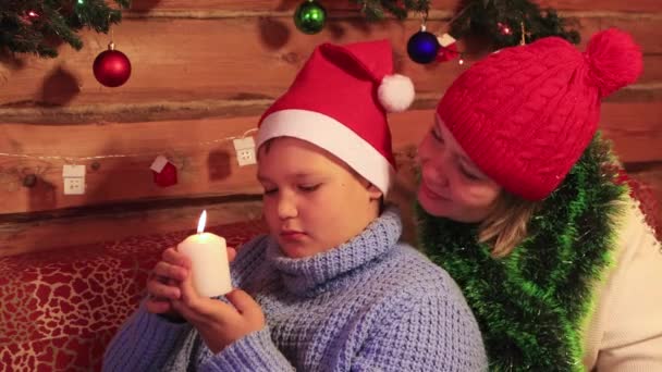 Μαμά και γιος σε κόκκινα καπέλα εξετάσει ένα λευκό κερί Χριστουγέννων. — Αρχείο Βίντεο