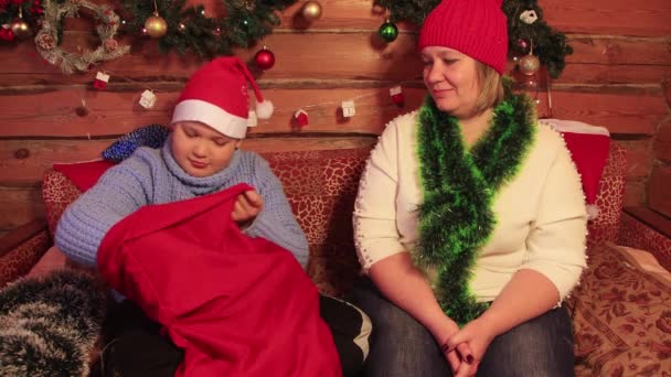 Un niño con un sombrero rojo de Santa Claus toma un regalo de Navidad de una bolsa. — Vídeos de Stock