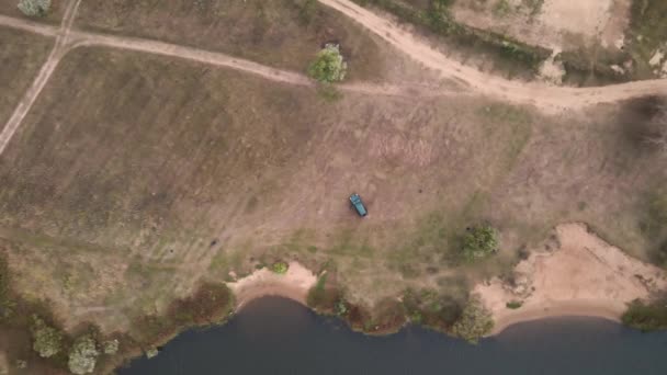 Volando sobre un amplio campo con un coche aparcado junto al lago. — Vídeos de Stock