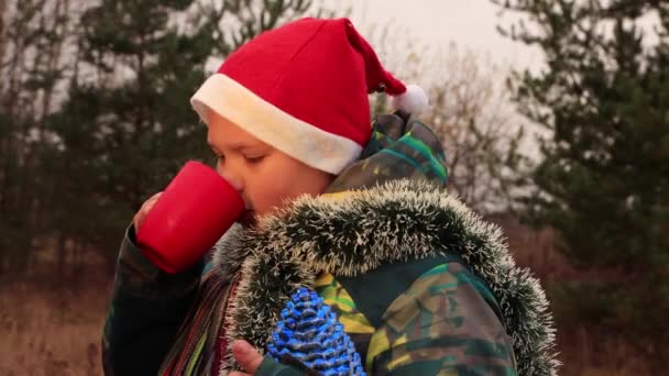 Op kerstavond drinkt de jongen uit een rode beker en lacht hij.. — Stockvideo