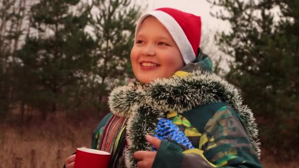 In der Weihnachtsnacht lächelt der Junge und hält eine rote Tasse und eine große Beule in der Hand. — Stockvideo