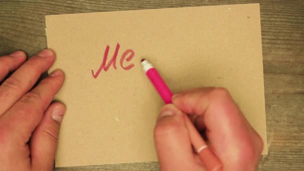 A mans hand writes a red felt-tip pen on a cardboard sheet Merry Xmas. — Stock Video